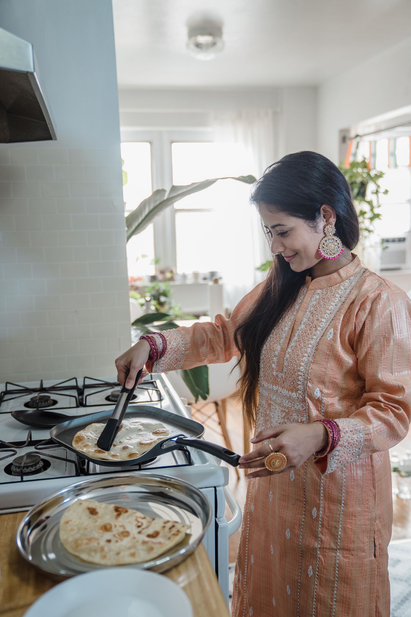 A woman cooking paratha in a home kitchen